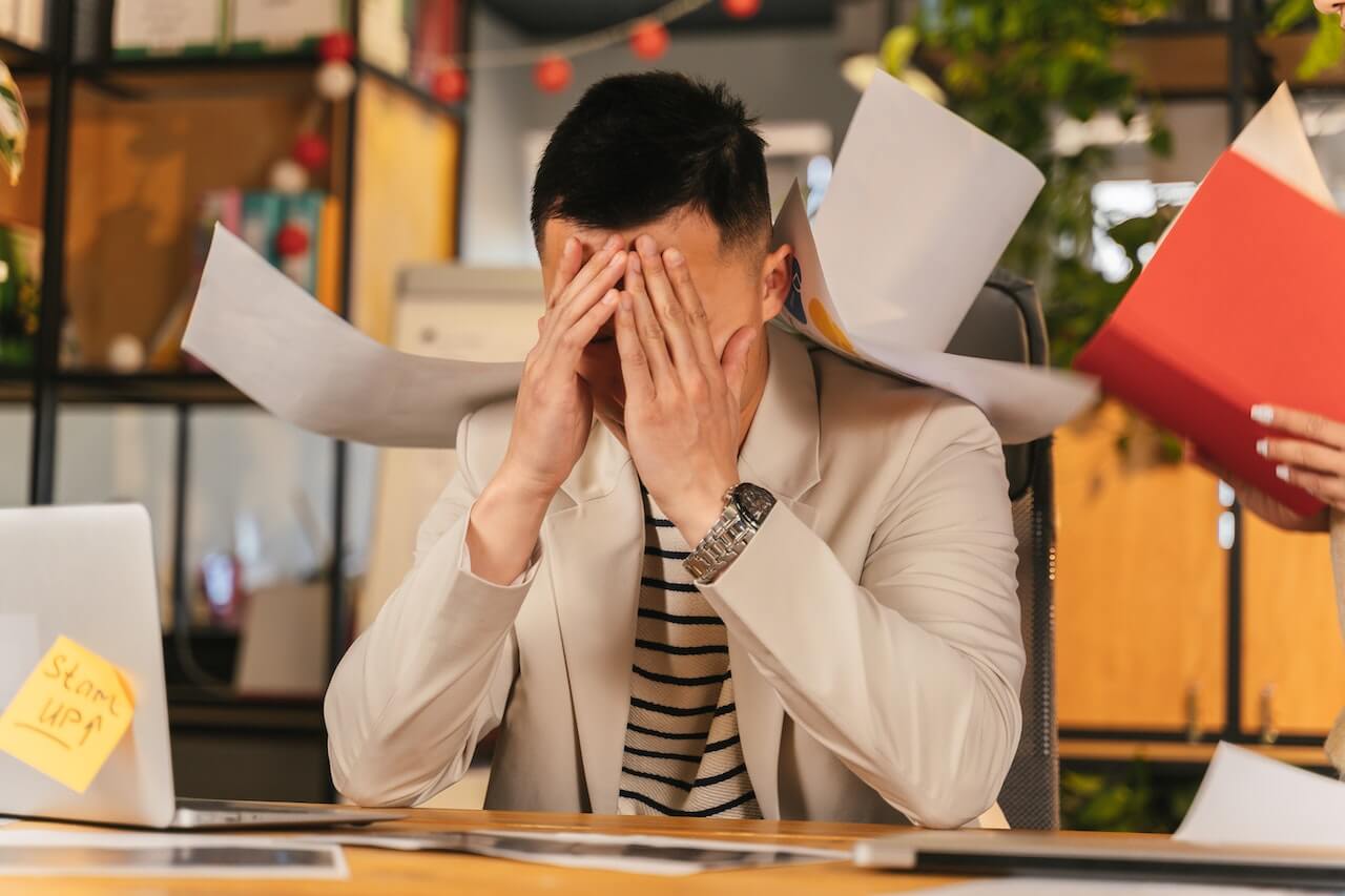 a man in a suit covering his face while papers are floating around him